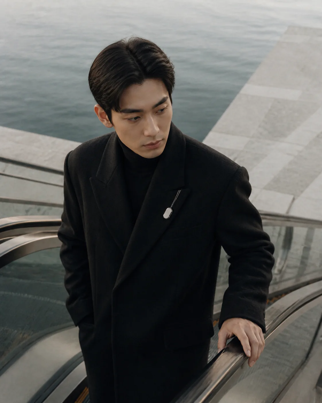 Person wearing Presence Key on a black lapel while riding an escalator