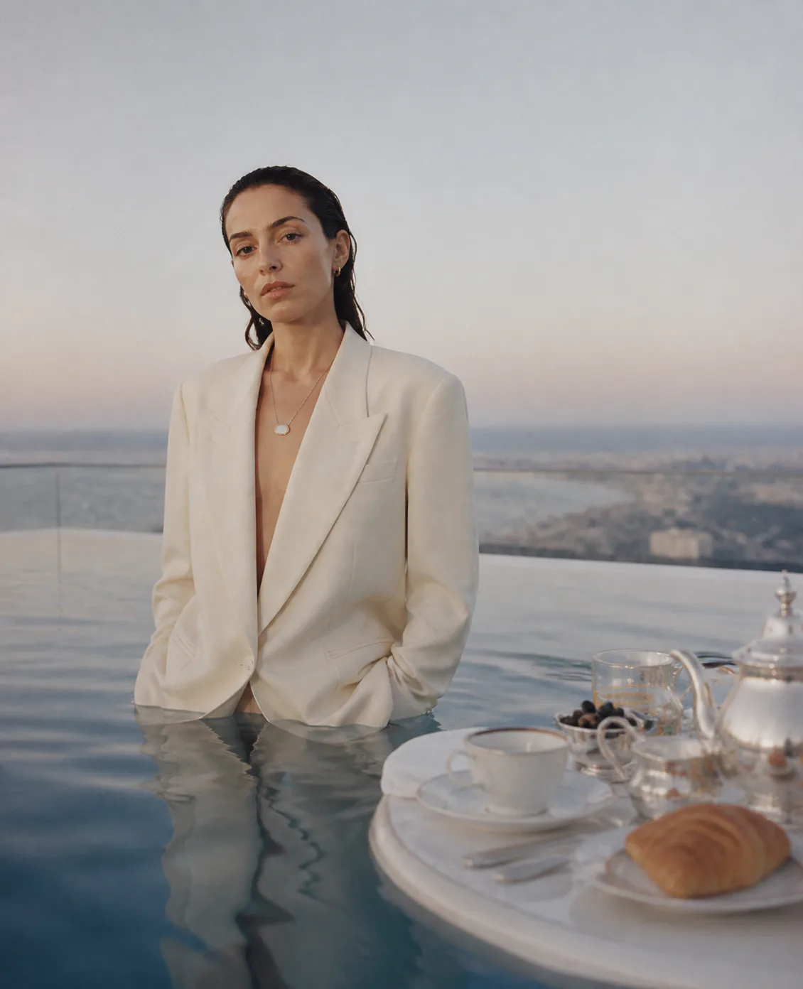 Woman wearing an ivory Presence Key beside a poolside breakfast